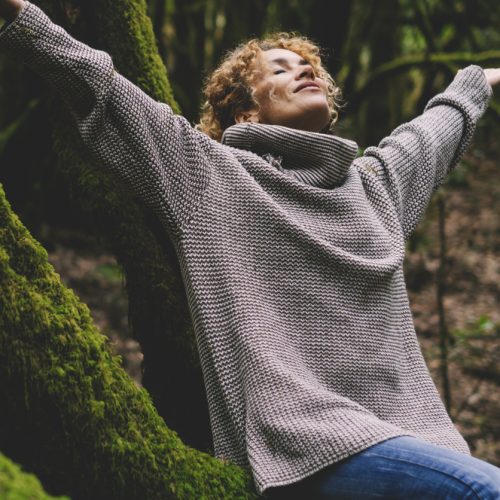 Woman happy in outdoor leisure activity. Celebrating healthy lifestyle people and freedom. Earth's day. Woman sitting and outstretching arms in the forest with green trees trunk in background. Forest