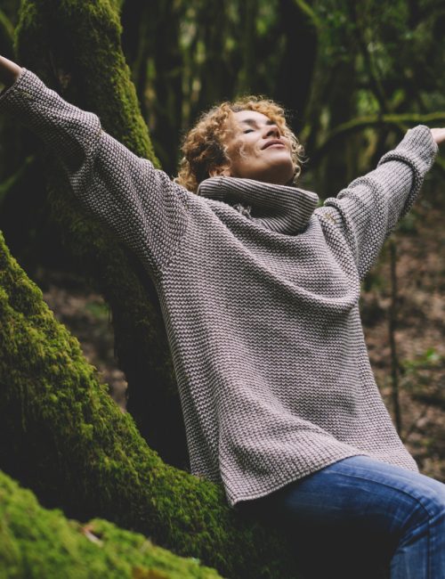 Woman happy in outdoor leisure activity. Celebrating healthy lifestyle people and freedom. Earth's day. Woman sitting and outstretching arms in the forest with green trees trunk in background. Forest